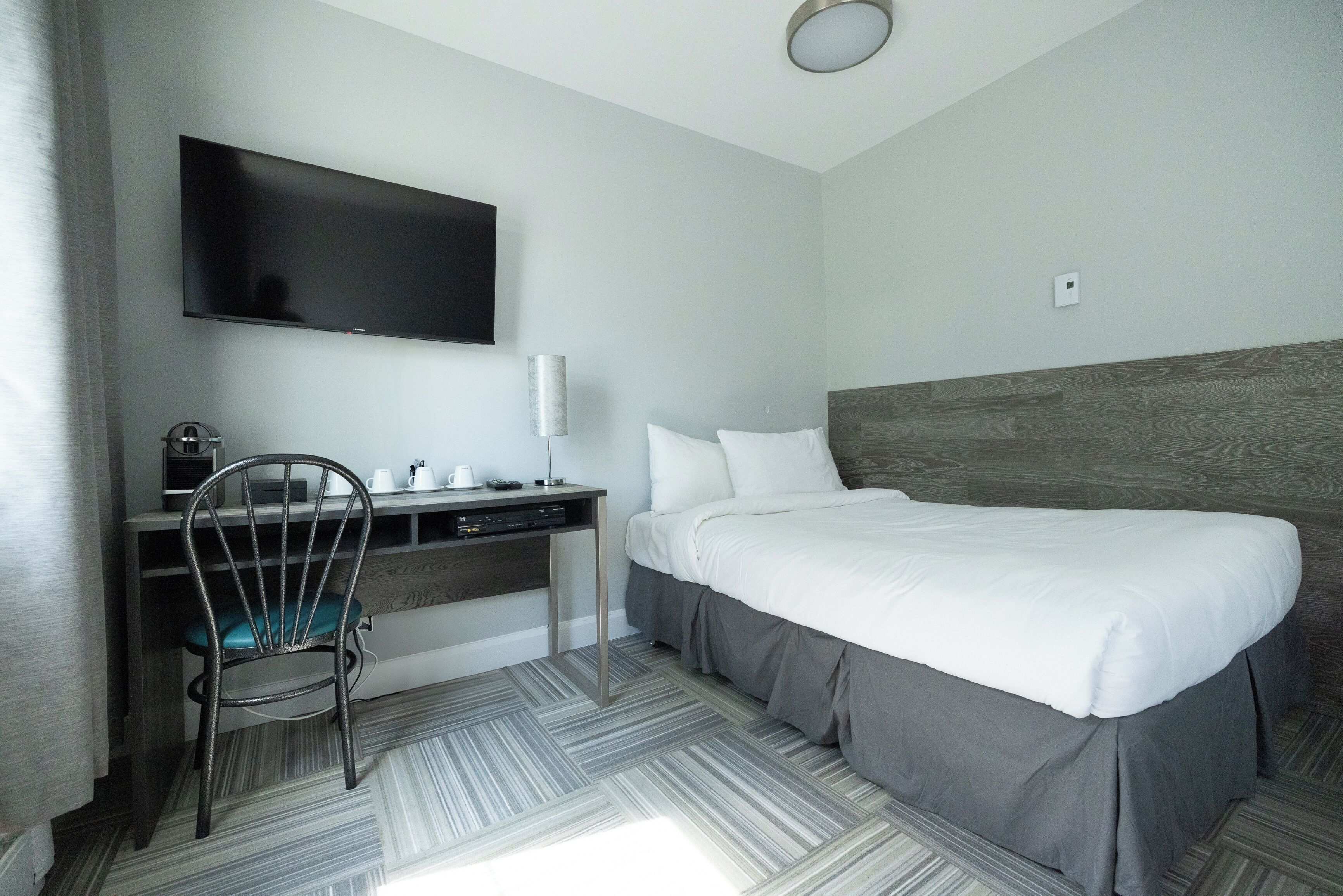 A hotel room with a bed, a desk with a chair, a flat-screen TV, and a lamp.