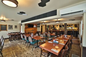 Um restaurante com mesas e cadeiras de madeira, um espaço de bar e um aparelho de ar condicionado no teto.