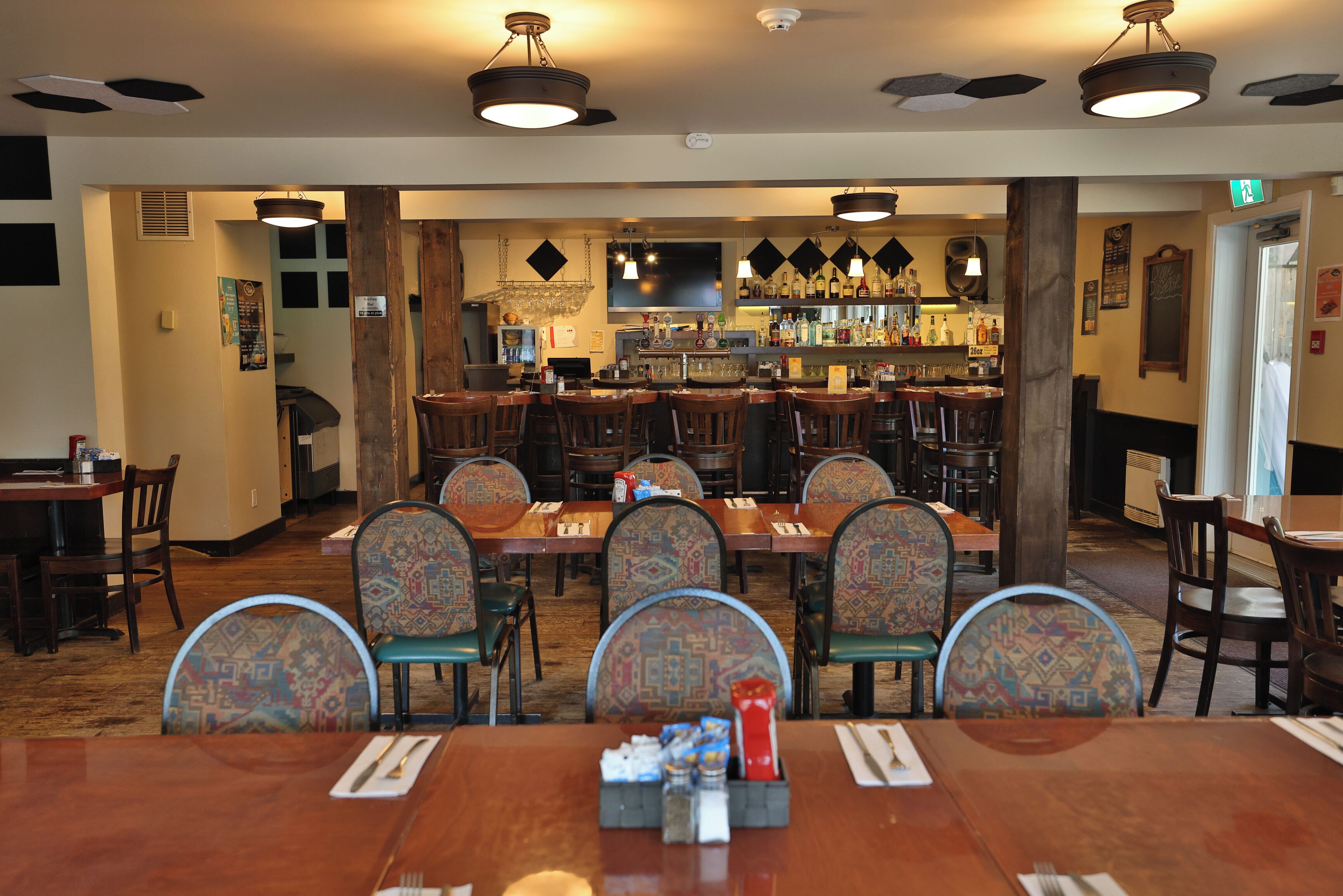 A restaurant with a bar area, wooden tables, and patterned chairs.
