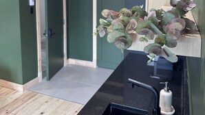 Et moderne badeværelse med bordplade i sort, vask og en plante på en hylde.