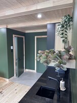 Casa de banho moderna com bancada preta, lavatório e uma planta numa prateleira.