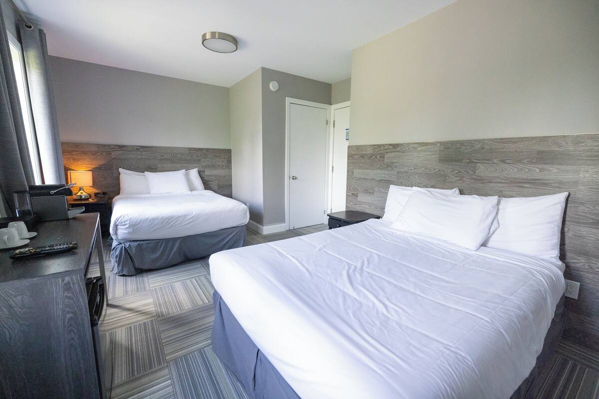 A hotel room with two beds, a desk with a lamp, and a TV.