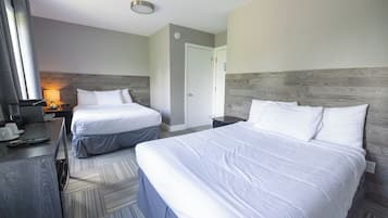 A hotel room with two beds, a desk with a lamp, and a TV.