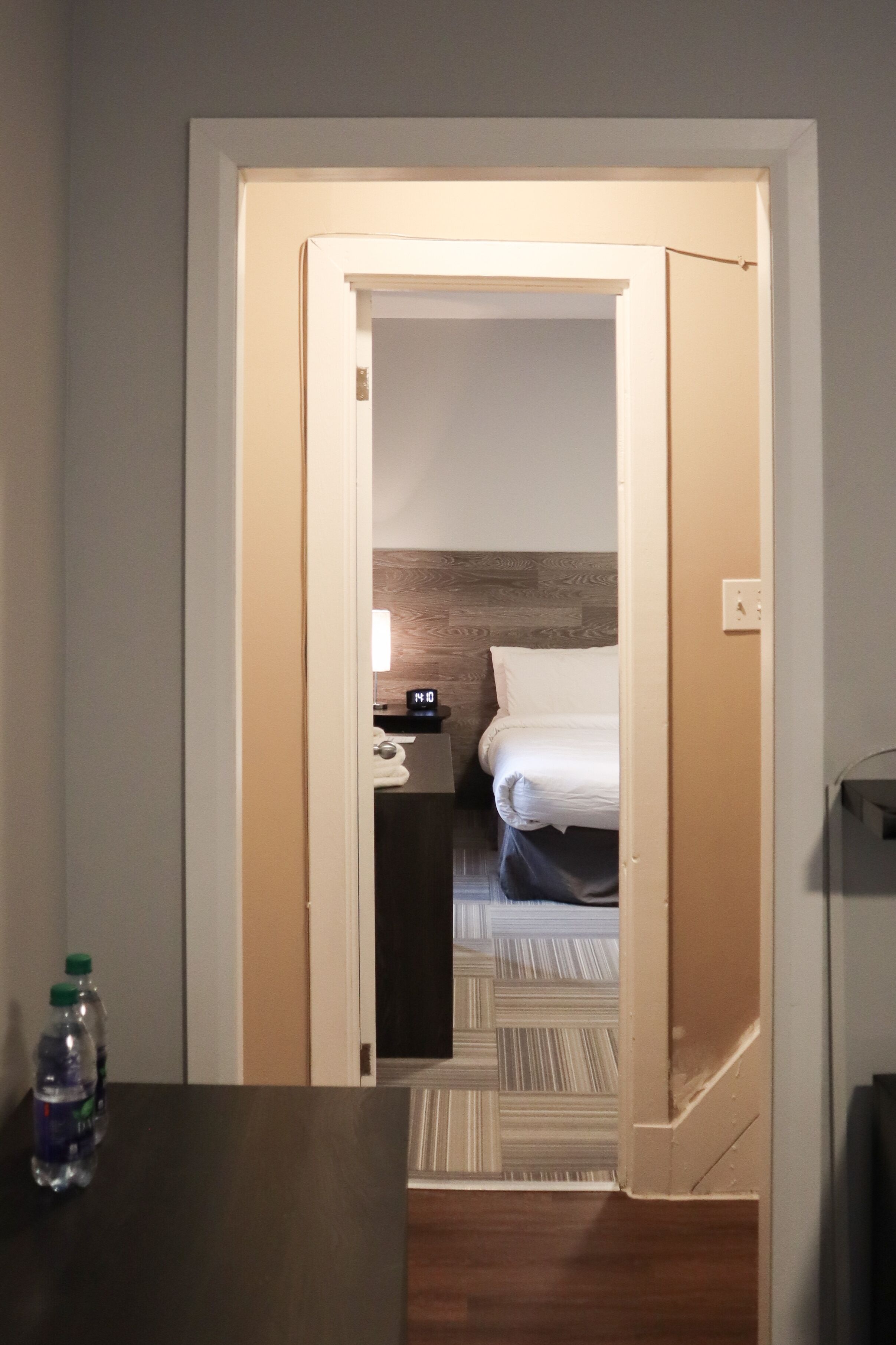 A hotel room with a bed, a nightstand, and a water bottle on a table.