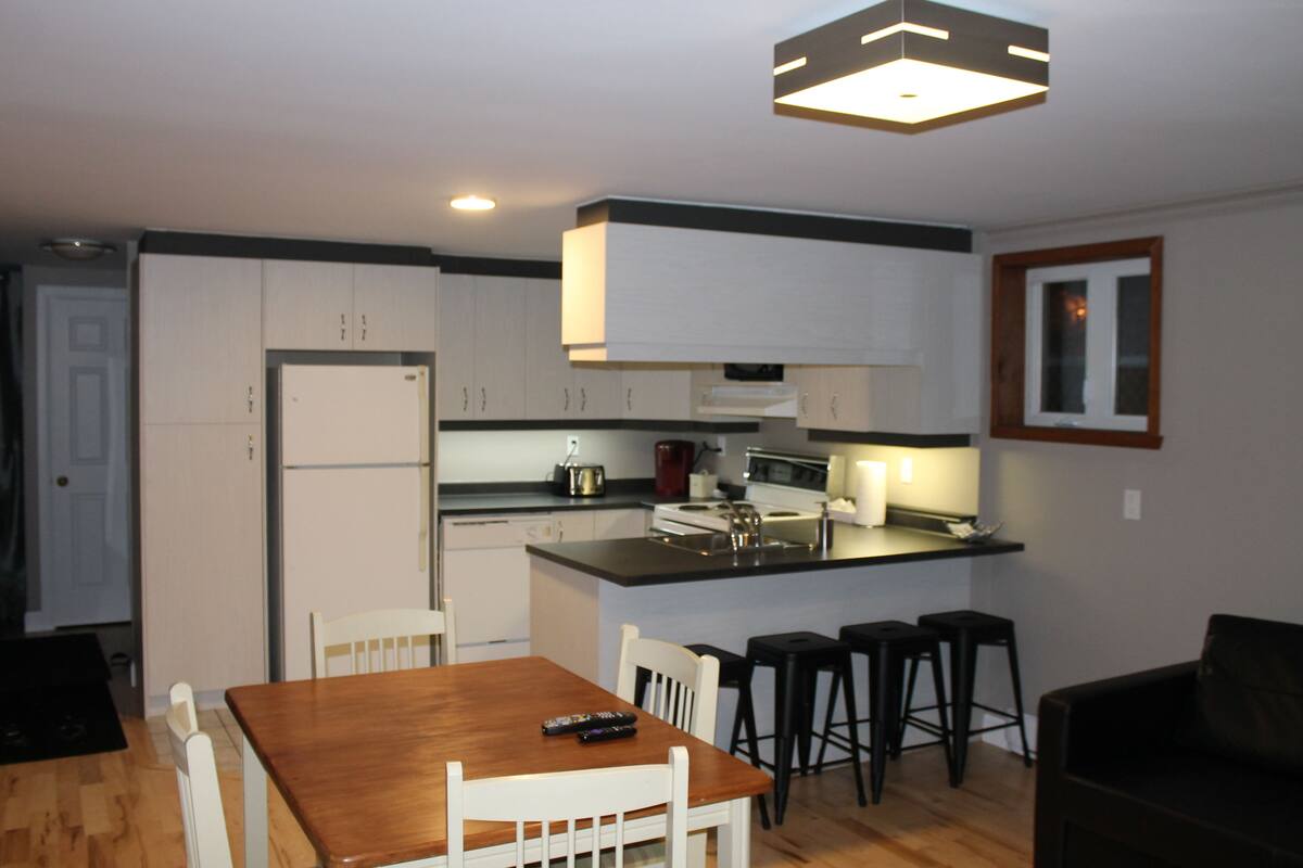 A compact kitchen with white cabinets, a wooden dining table, and black bar stools.