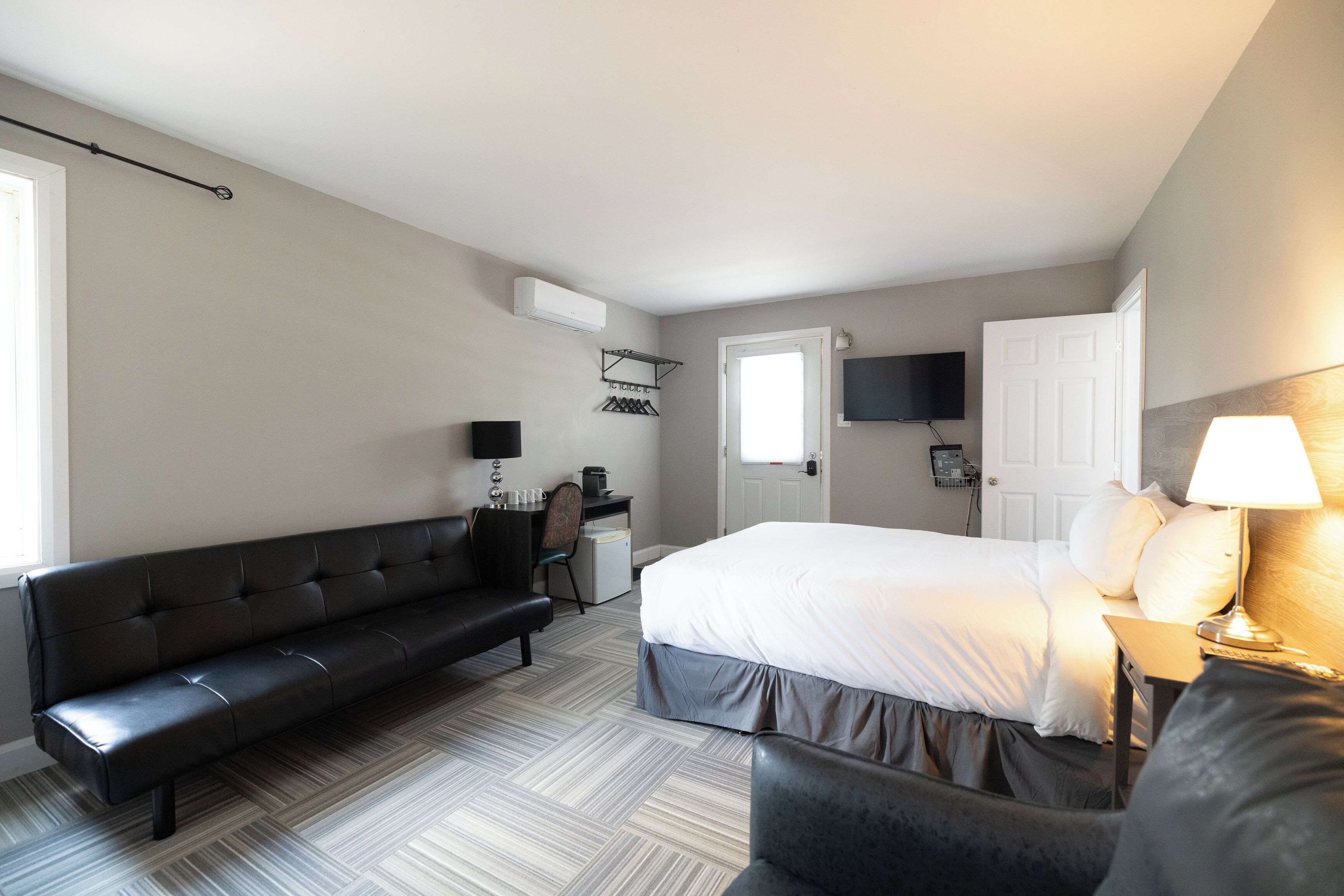 A hotel room with a bed, a sofa, a desk, a chair, a TV, and a lamp.
