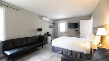 A hotel room with a bed, a sofa, a desk, a chair, a TV, and a lamp.