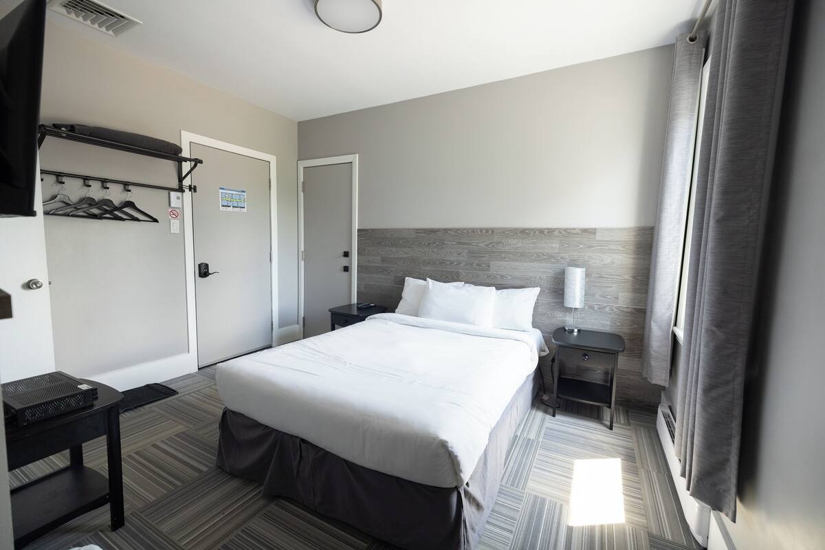 A hotel room with a large bed, a bedside table, a nightstand, a coat rack, and a shower curtain.