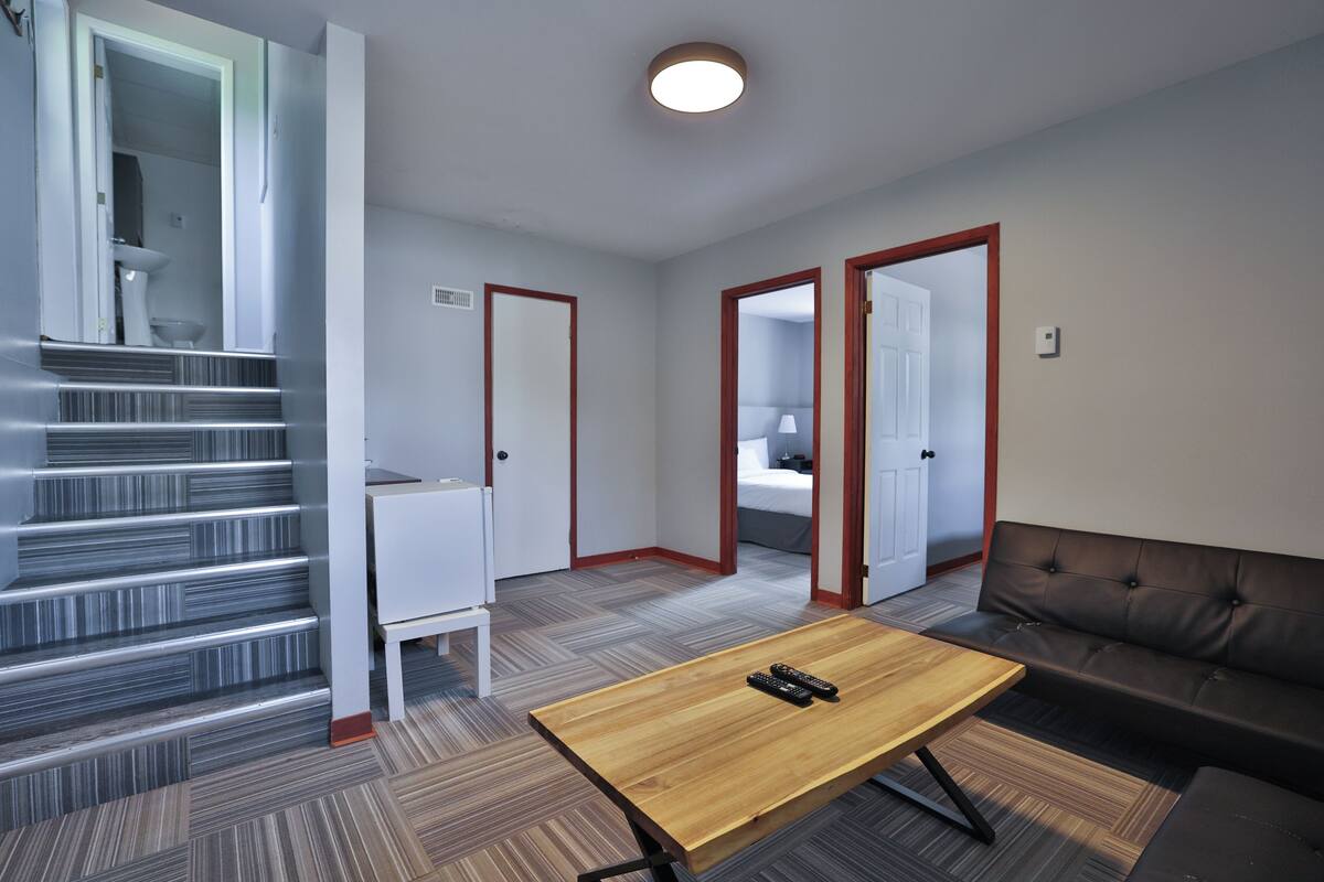 A modern hotel room with a wooden table, a sofa, and a staircase leading to a bathroom.