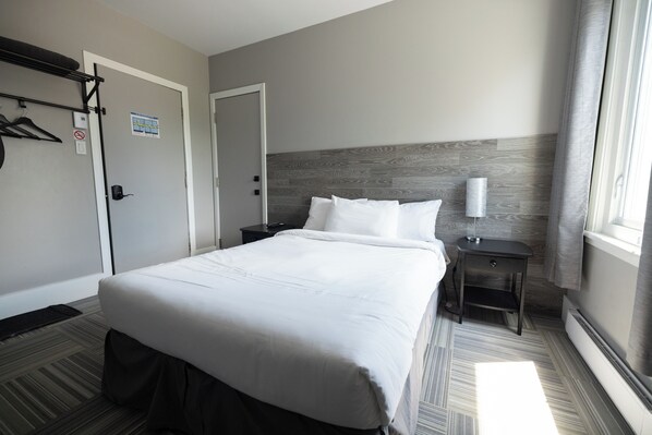 Habitación de hotel con una cama grande, una mesita de noche, una lámpara de pared y una ventana con cortinas.