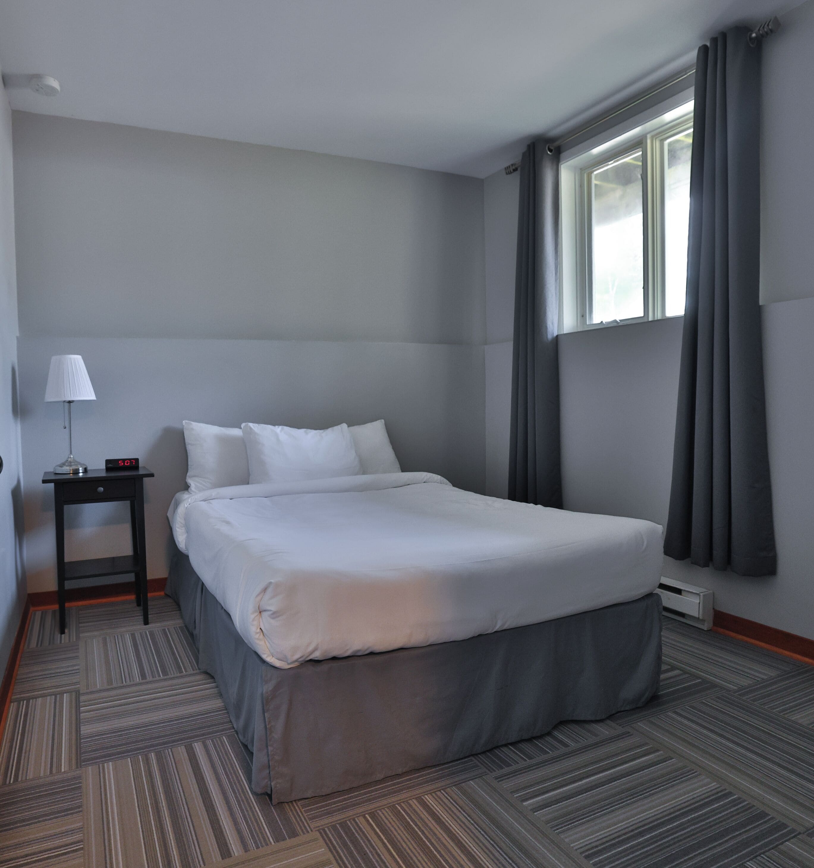 A hotel room with a large bed, a bedside table with a lamp, and a window with curtains.