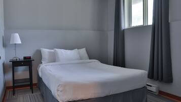 Quarto de hotel com uma cama grande, uma mesa de cabeceira com abajur e uma janela com cortinas.