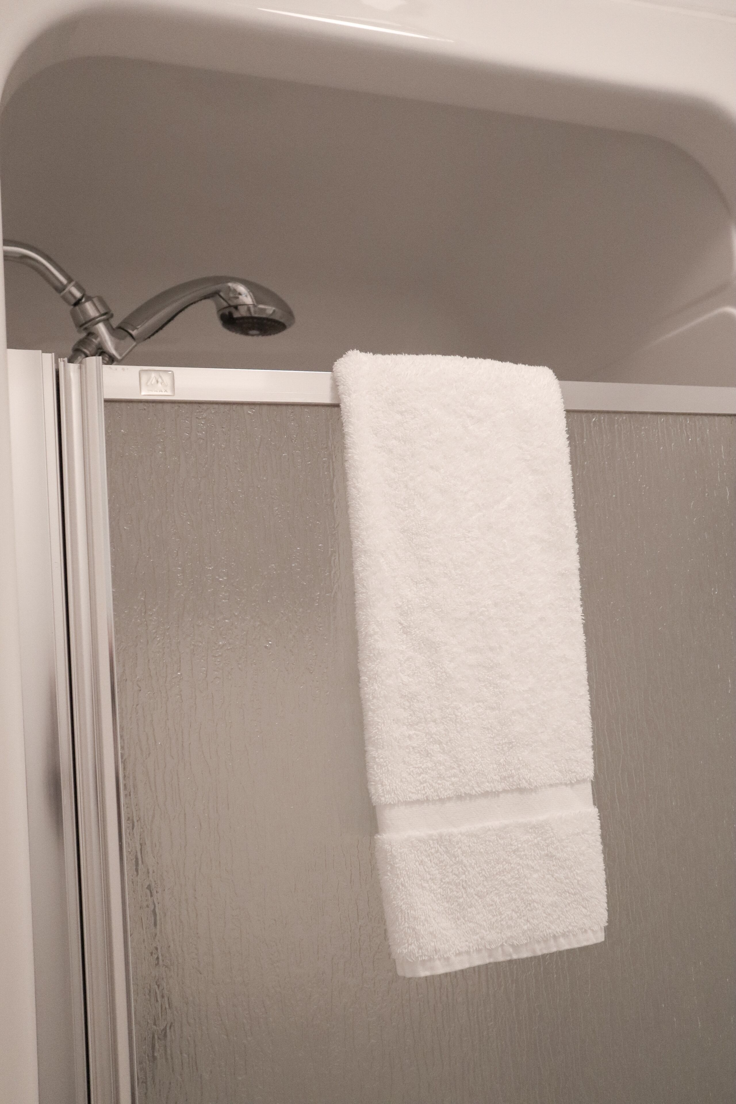 A white towel hanging on a shower door in a bathroom.