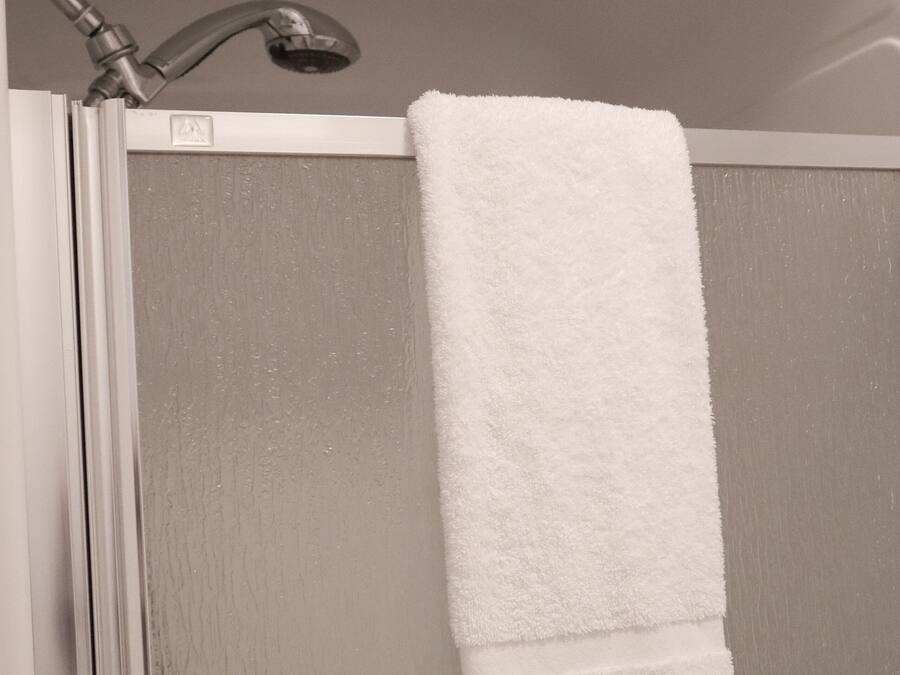 A white towel hanging on a shower door in a bathroom.