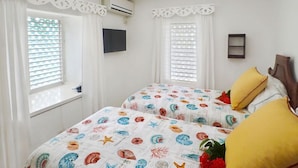 A room with two beds, white curtains, an air conditioning unit, a TV, and a small shelf. - Sea Spray 50 Steps to the Sea, Silver Sands, 3 BR (Duncans)