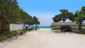 A beach view with a sandy path leading to a building with a thatched roof. - Sea Spray 50 Steps to the Sea, Silver Sands, 3 BR (Duncans)