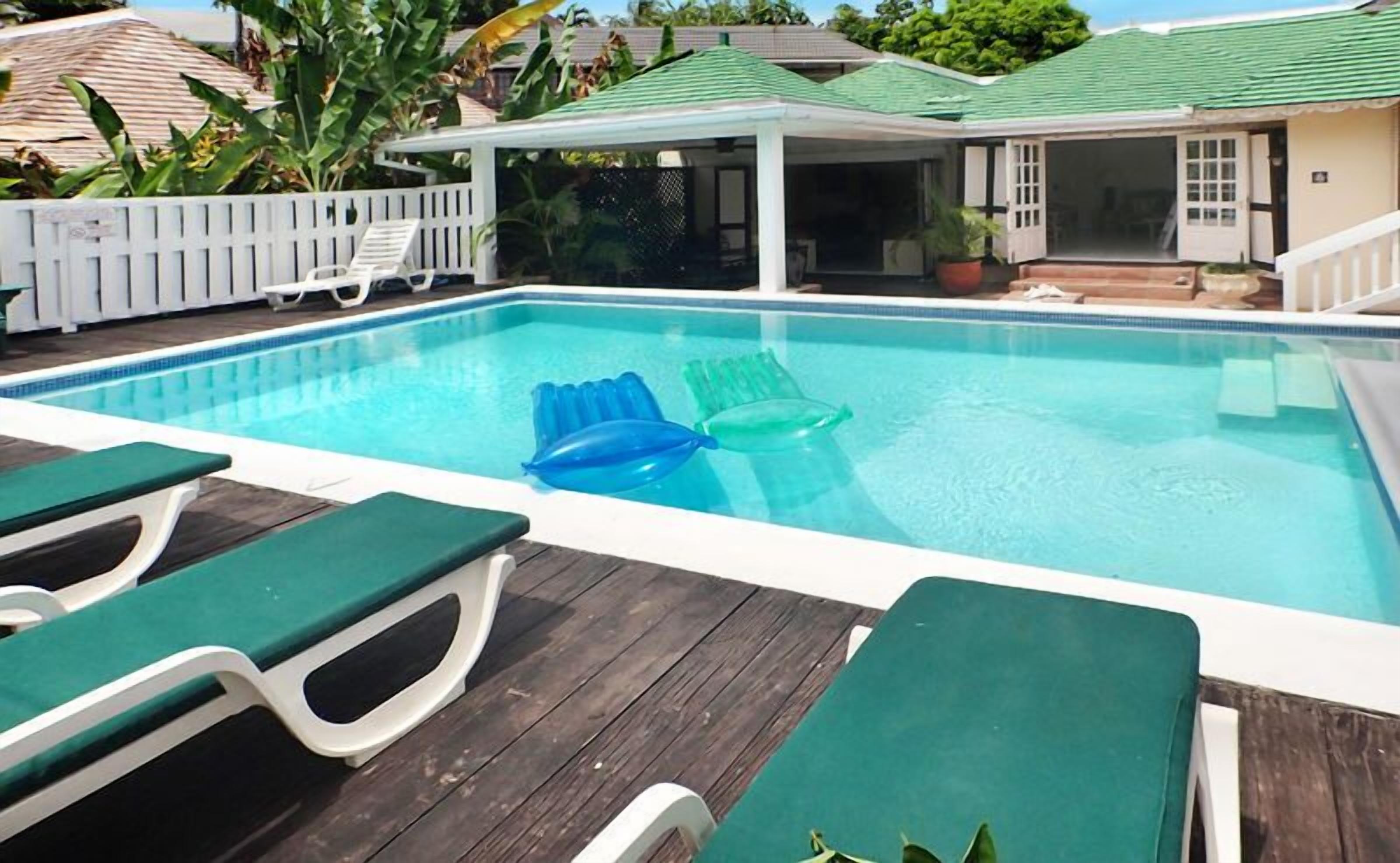 A swimming pool with green lounge chairs and a covered patio area.