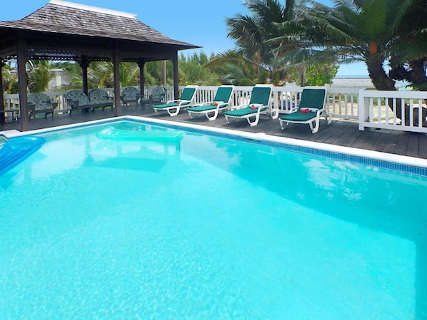 A clear blue pool with lounge chairs and a gazebo.