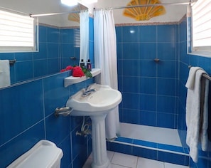 A bathroom with blue tiles, a pedestal sink, a shower with a curtain, and a toilet.