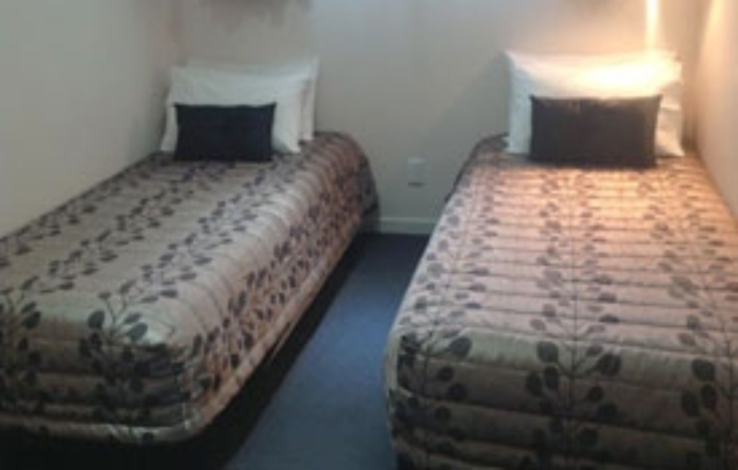 Two single beds with floral bedding, a small bedside table, and a wall-mounted light.