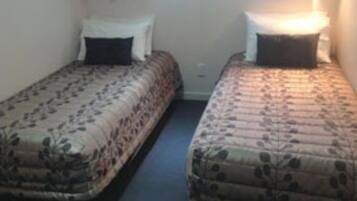Two single beds with floral bedding, a small bedside table, and a wall-mounted light.