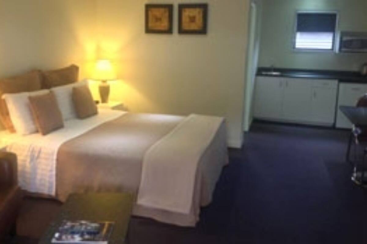 Una habitación de hotel con cama, mesitas de noche, escritorio y kitchenette.