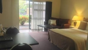 Une chambre d’hôtel avec un lit, un bureau, une chaise, un canapé et une table. Il y a une fenêtre donnant sur un paysage verdoyant.