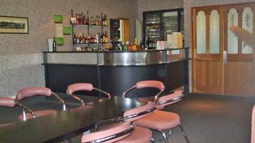 Eine Bar mit einer Theke und Regalen voller Flaschen, ein Tisch mit rosa Stühlen und eine Tür mit satinierten Glasscheiben.
