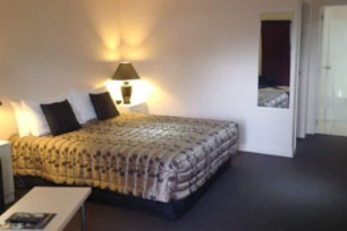 Una habitación de hotel con una cama, una mesita de noche, una lámpara y una puerta.