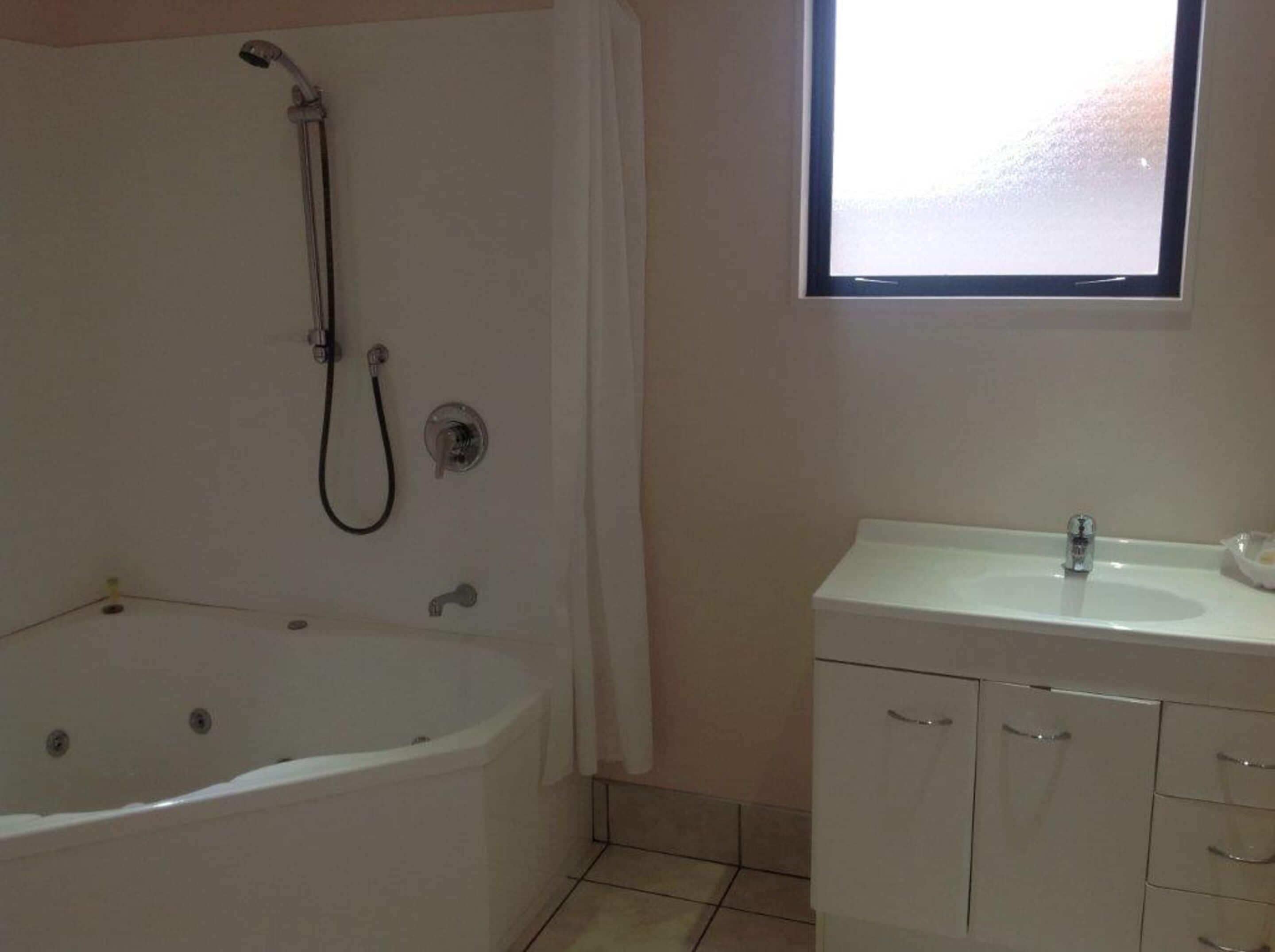 A bathroom with a bathtub, a shower, a sink, and a window.