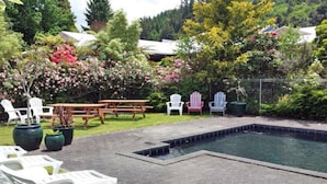 Un jardin avec une piscine, des tables de pique-nique et des fauteuils Adirondack.
