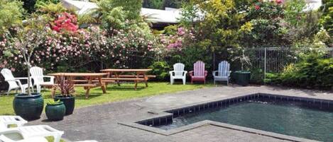 Un patio trasero con piscina, mesas de picnic y sillas Adirondack.
