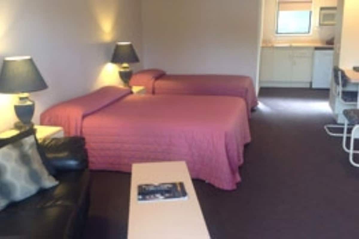 Habitación de hotel con dos camas, un escritorio, una silla y una pequeña cocina.