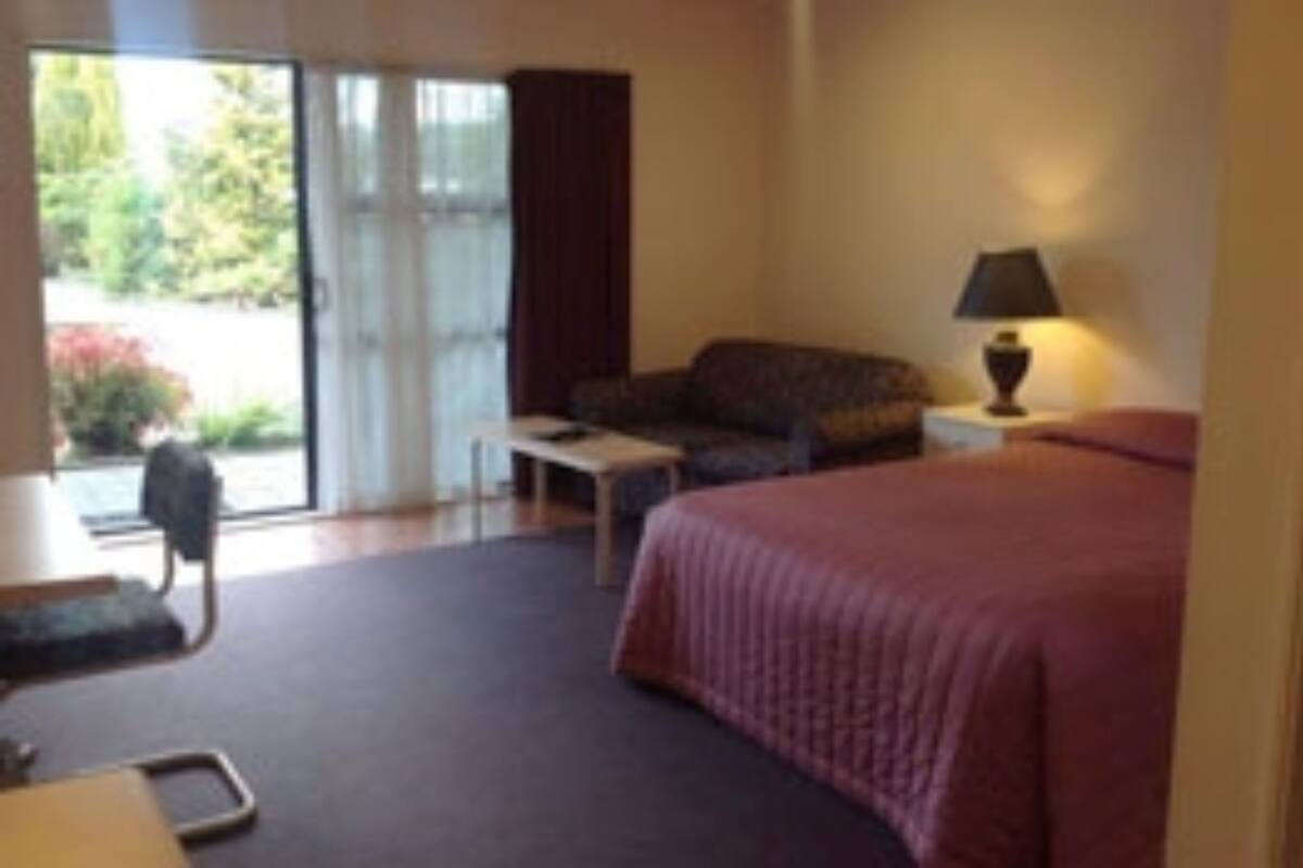 Habitación de hotel con cama, sofá, una mesita, lámpara y puerta corrediza de vidrio que da a un jardín.