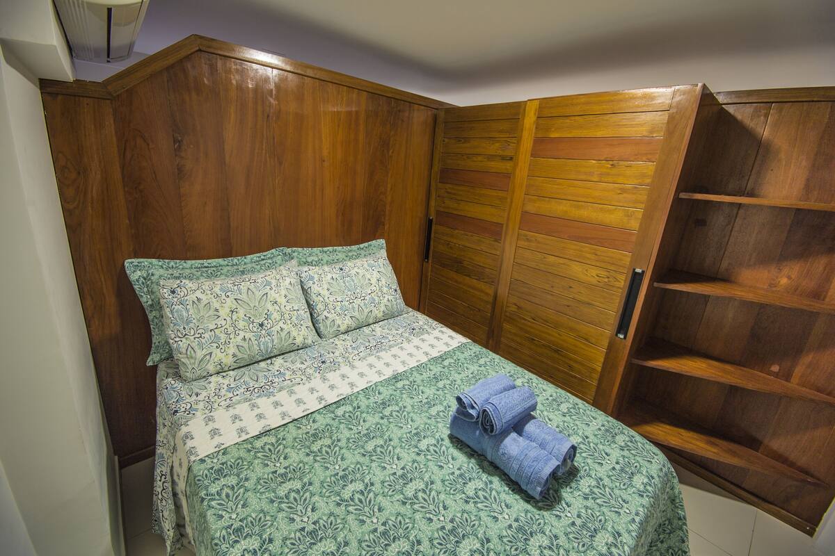 Un dormitorio con un armario de madera, una cama con ropa de cama estampada y un par de toallas enrolladas sobre la cama.