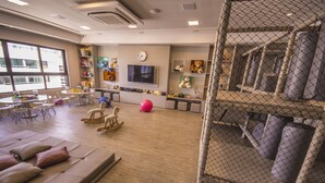 Zona de juegos para niños con televisor, juguetes y asientos cómodos.