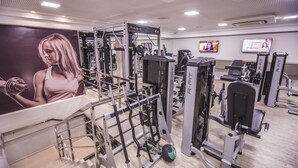 Un gimnasio con diferentes máquinas de ejercicio, un cartel grande y dos televisores en la pared.