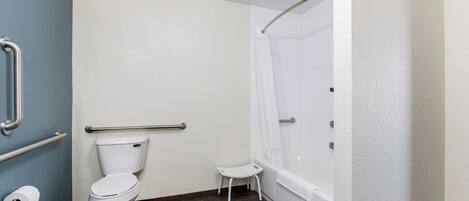 Ein Badezimmer mit Toilette, einer kleinen Stehgehilfe, einer Dusche mit weißem Duschvorhang und einer Handstange.