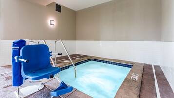 Una piscina con una silla azul y una escalera, suelo de baldosas y un aplique en la pared.