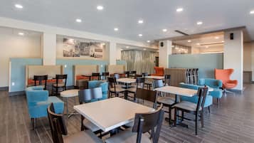 A modern dining area with multiple tables and chairs, a reception desk, and a decorative wall with a cityscape.