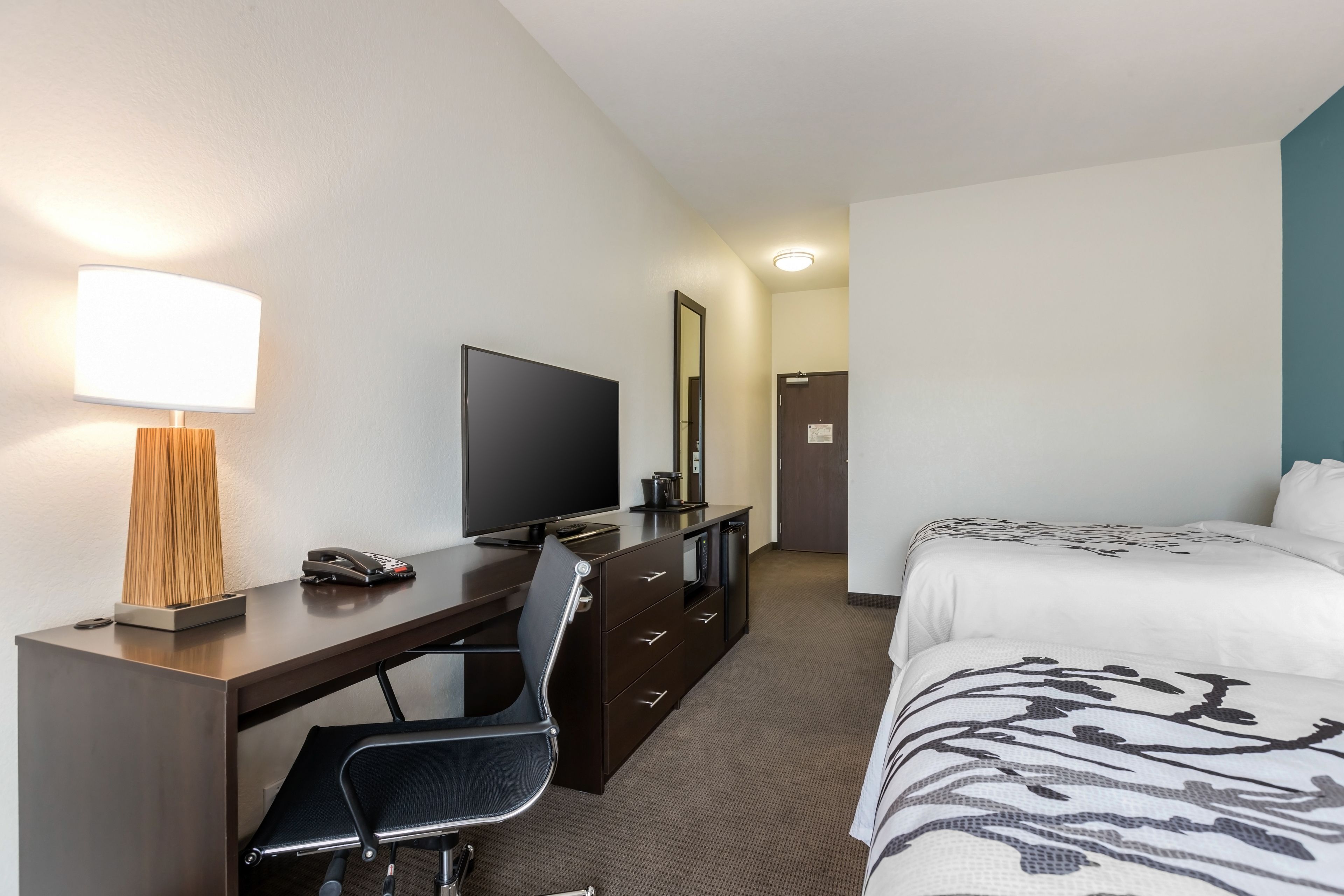 A hotel room with a desk, a television, a bed with patterned bedding, a chair, and a lamp.