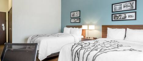 A hotel room with two beds, a desk, and a chair. There are framed pictures on the wall.