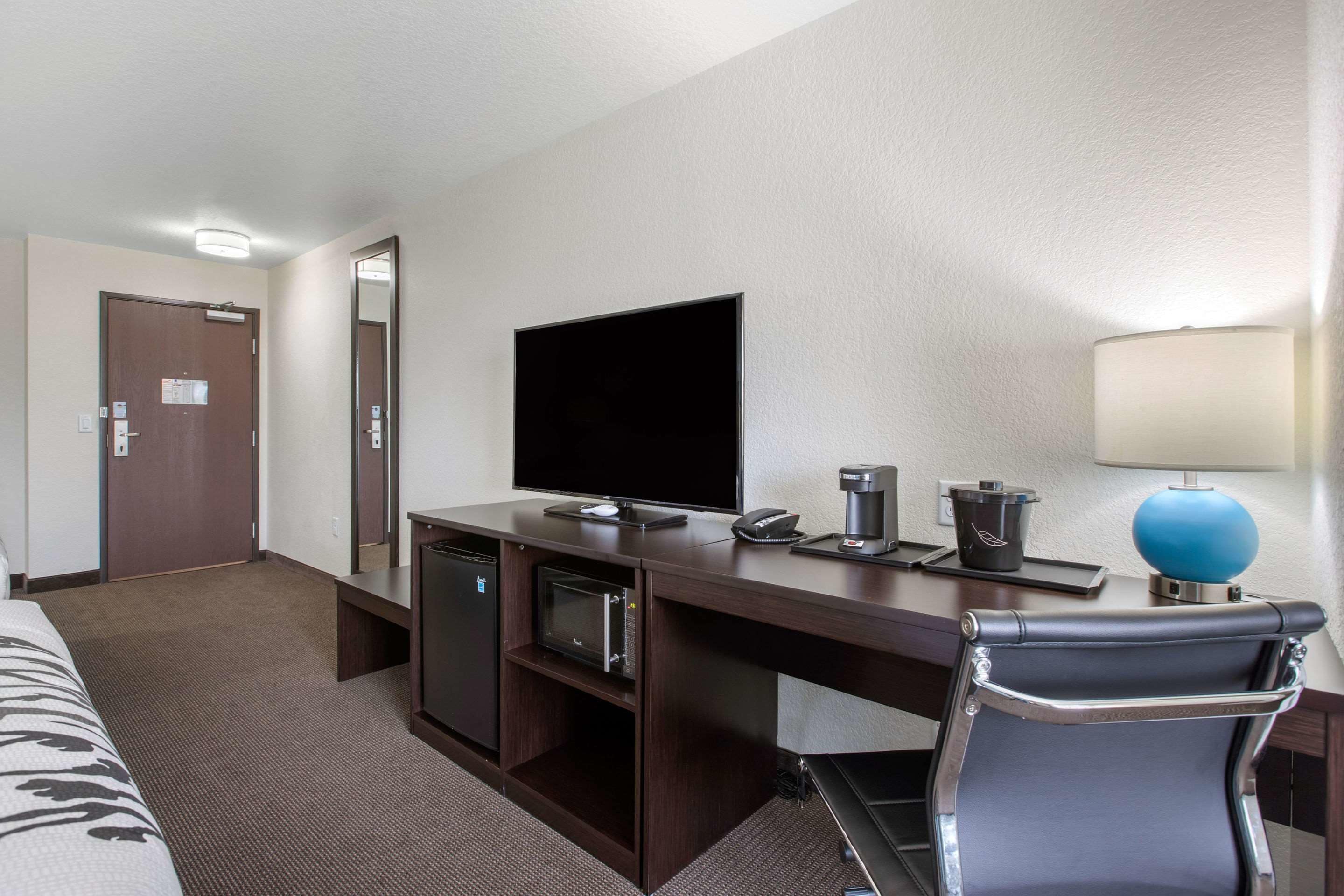 A hotel room with a bed, a desk with a flat-screen TV, a coffee maker, a lamp, and a microwave.