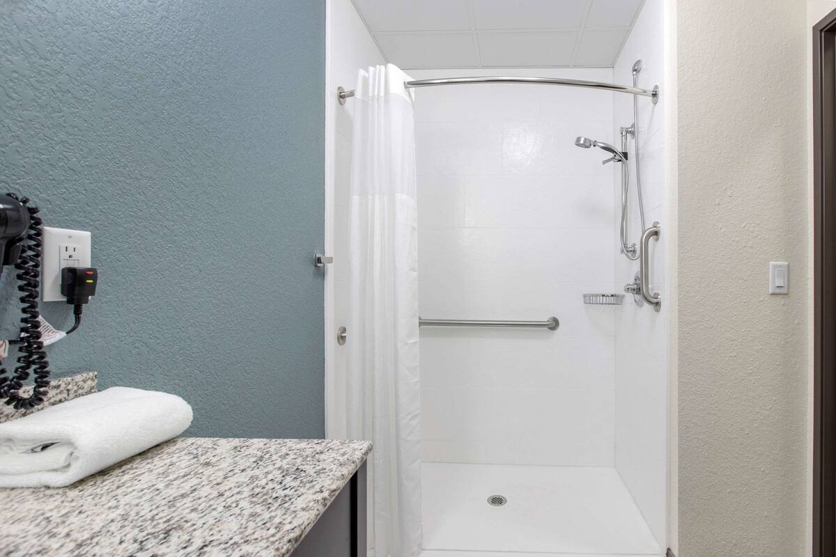 A bathroom with a shower, a towel on the counter, and a phone charger.