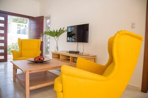 A living room with two yellow armchairs, a wooden coffee table, and a flat-screen TV on the wall.
