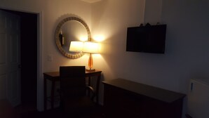 Una stanza con una scrivania, una sedia, una lampada e un televisore montato a parete.
