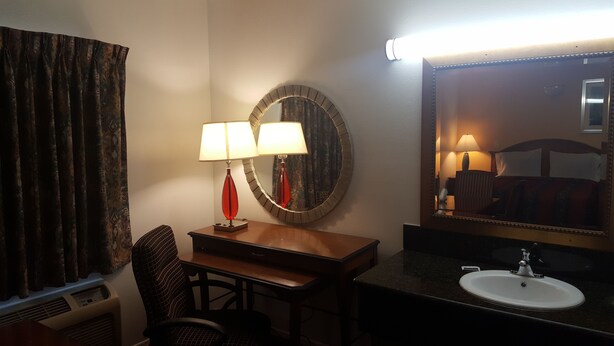Una camera d'albergo con una scrivania, due lampade, uno specchio, una sedia e un lavandino.