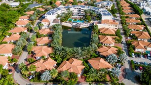 Vista aérea de un resort con piscina central, rodeado de villas de techo rojo y palmeras.