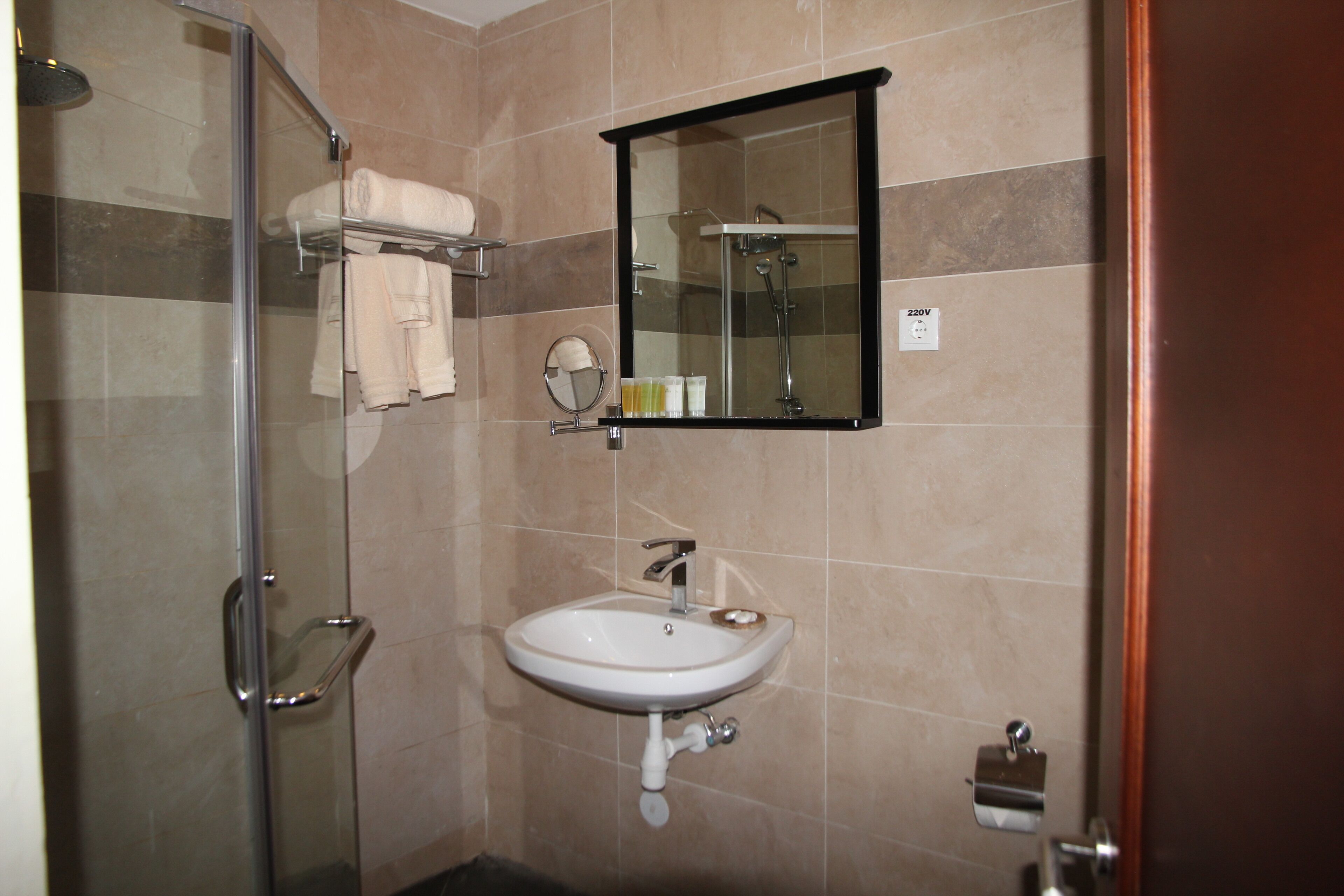 Un baño con cabina de ducha de vidrio, un lavabo con espejo y un perchero con toallas.