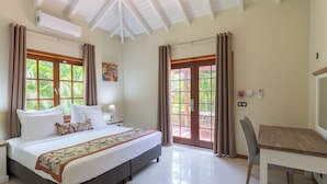 Un dormitorio amplio con una cama grande, un escritorio de madera y vistas a la vegetación por las ventanas.